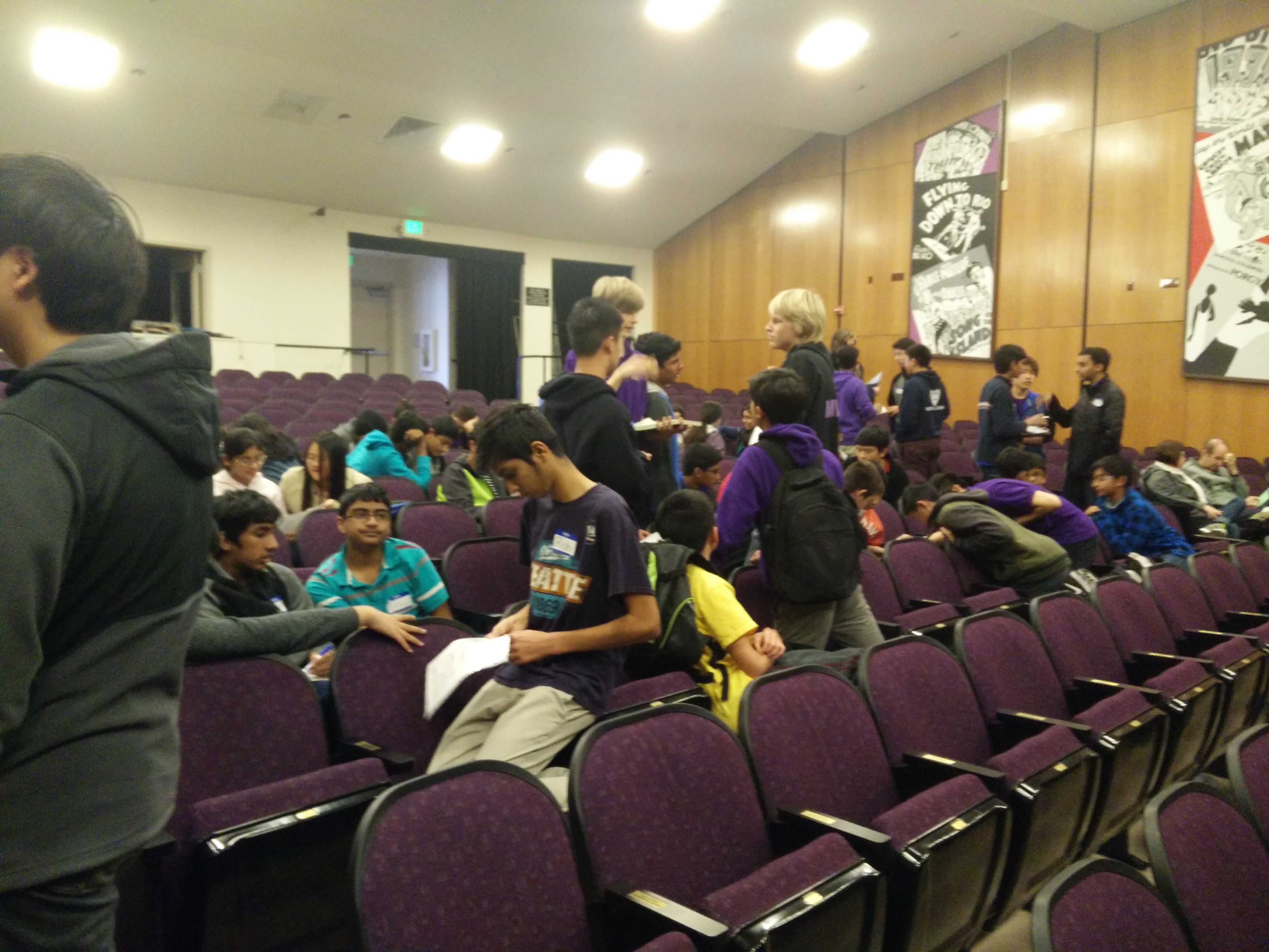 Robotics team members exchange strategies in small groups in the auditorium.