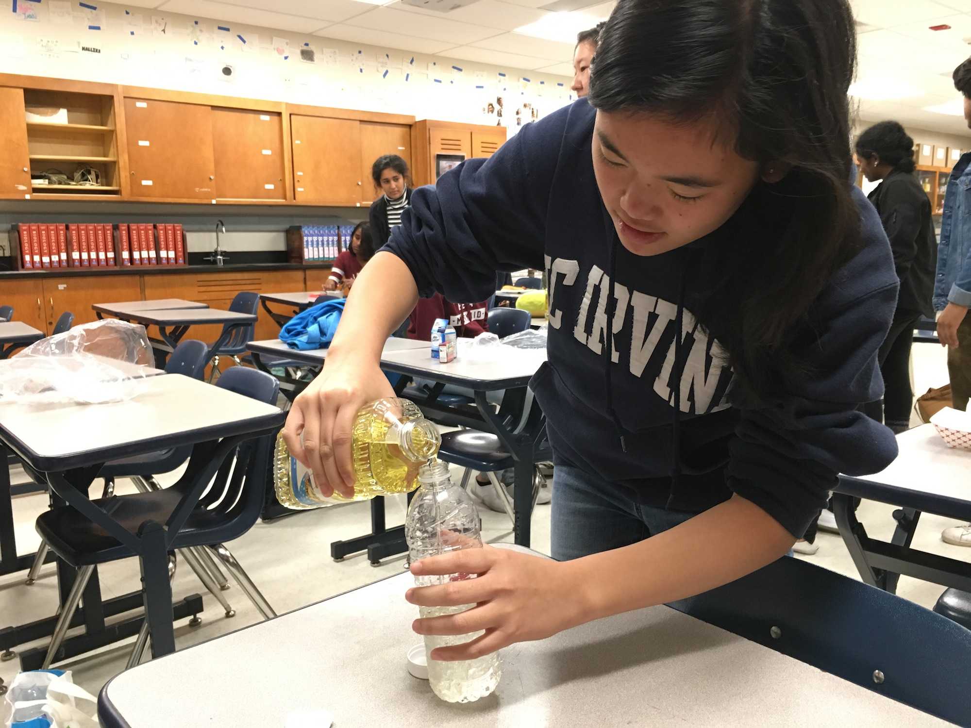 Senior Rochelle Tham pours oil into an empty water bottle to create the base for her lava lamp. The mixture of water and oil helped create the bubbling effect of a lava lamp. Photo by Andrea Schlitt.